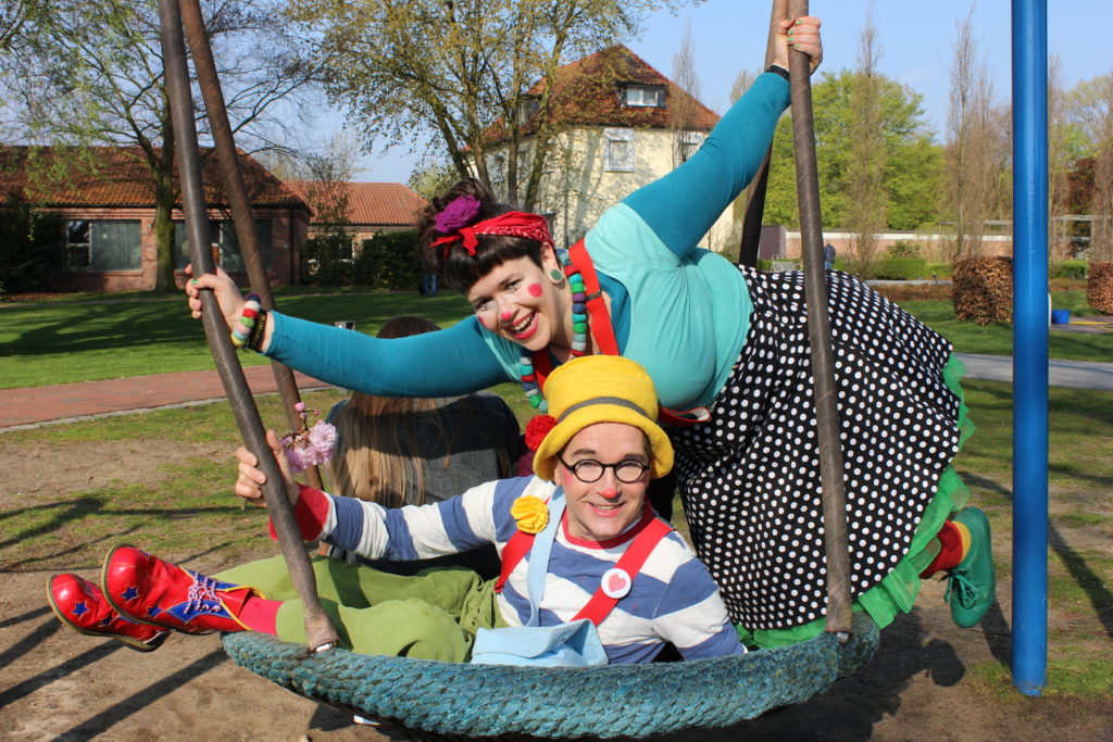 Ein Mann und eine Frau in Clownsverkleidung auf einer Schaukel