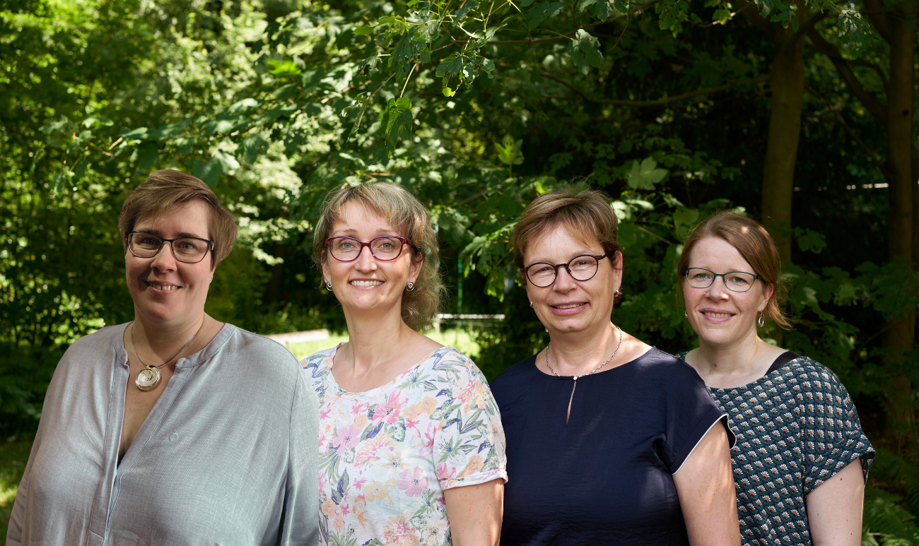Vier weibliche Personen, die im Familienbüro als Team arbeiten stehen als Gruppe nebeneinander.